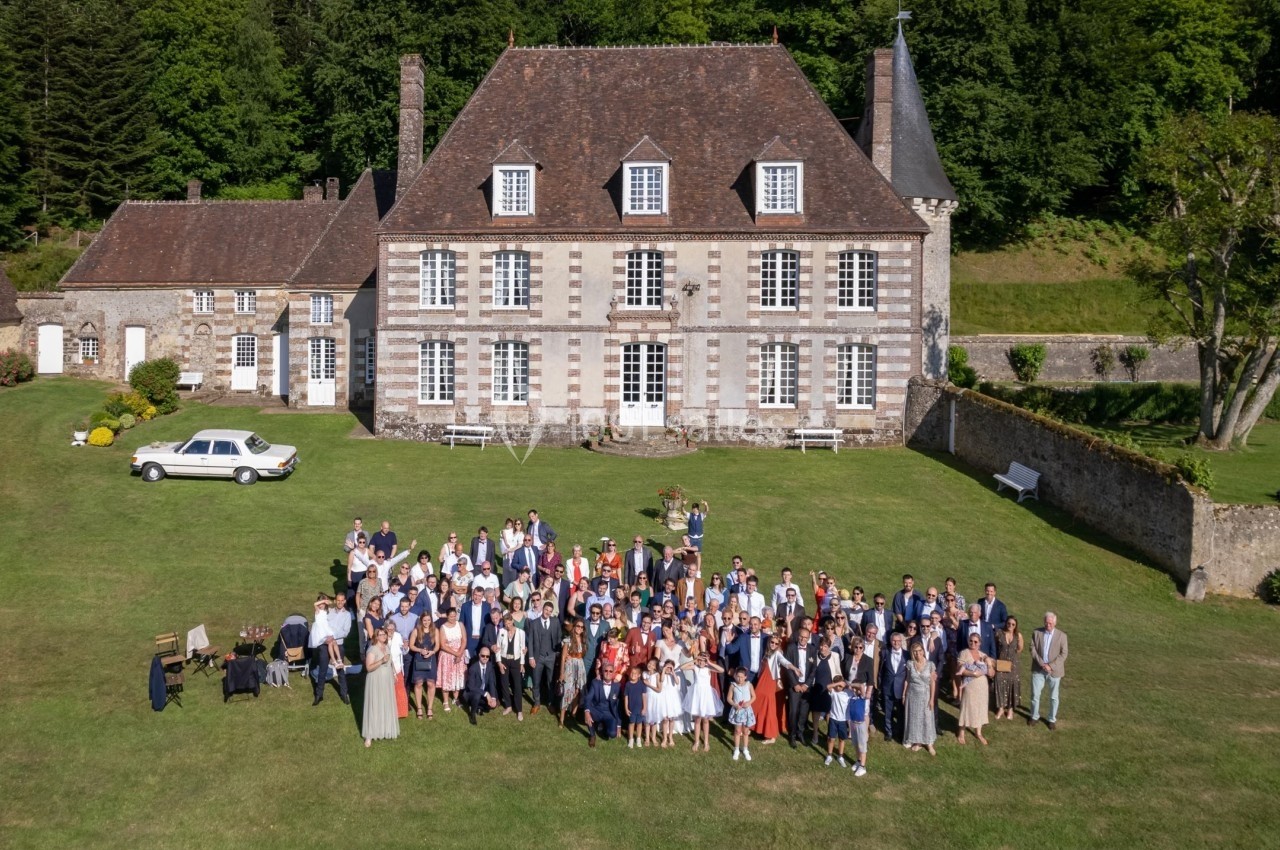 Groupe de personnes rassemblées devant un grand manoir en pierre avec un jardin verdoyant.