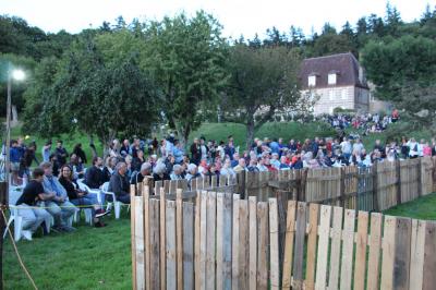 Salon rustique avec murs en pierre, canapés en cuir, table basse et porte ouverte donnant sur un jardin ensoleillé.