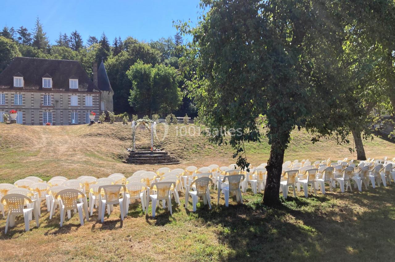 Chaises blanches disposées en rangées sur une pelouse, face à une arche décorative, avec un manoir en arrière-plan.