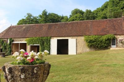 Salon rustique avec murs en pierre, canapés en cuir, table basse et porte ouverte donnant sur un jardin ensoleillé.