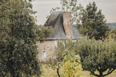 Salon rustique avec murs en pierre, canapés en cuir, table basse et porte ouverte donnant sur un jardin ensoleillé.