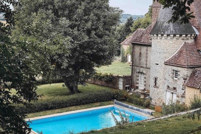 Salon rustique avec murs en pierre, canapés en cuir, table basse et porte ouverte donnant sur un jardin ensoleillé.