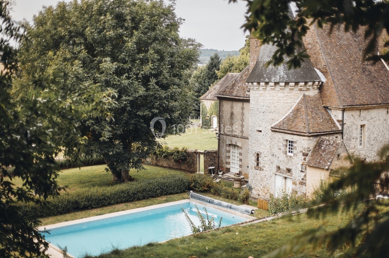 Vue d'une maison en pierre avec une piscine dans un jardin arboré, entourée de verdure.