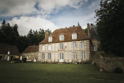 Salon rustique avec murs en pierre, canapés en cuir, table basse et porte ouverte donnant sur un jardin ensoleillé.