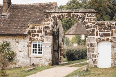 Salon rustique avec murs en pierre, canapés en cuir, table basse et porte ouverte donnant sur un jardin ensoleillé.