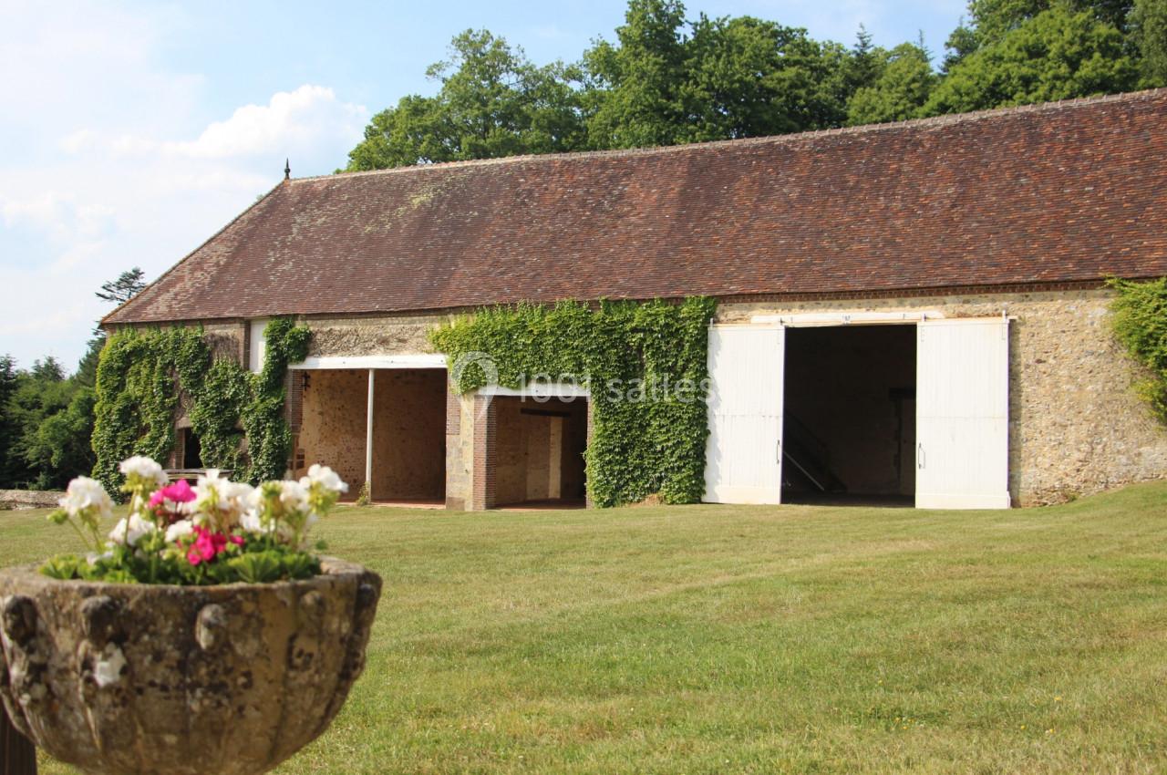 Grange en pierre avec toit en tuiles, portes blanches ouvertes et murs partiellement couverts de lierre, entourée de pelouse.