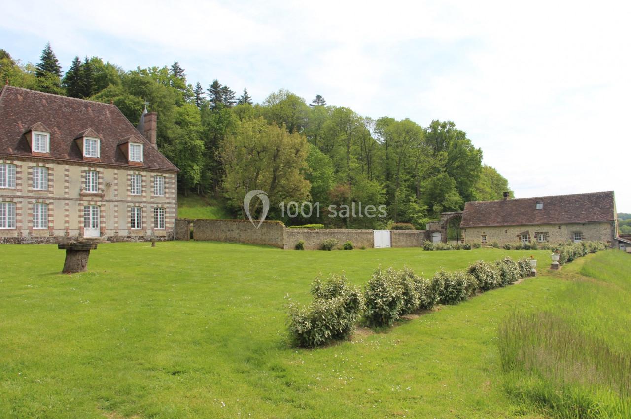 Grande maison en pierre avec toit en ardoise, entourée d'un jardin verdoyant et bordée d'arbres.