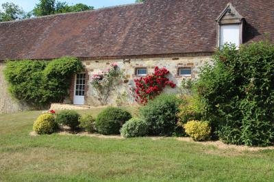 Salon rustique avec murs en pierre, canapés en cuir, table basse et porte ouverte donnant sur un jardin ensoleillé.
