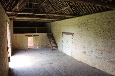 Salon rustique avec murs en pierre, canapés en cuir, table basse et porte ouverte donnant sur un jardin ensoleillé.