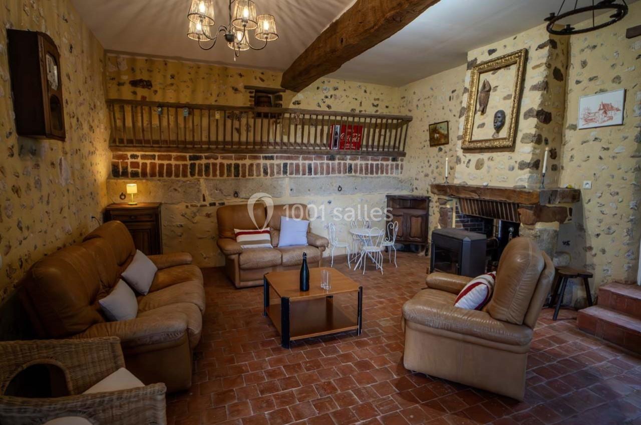 Salon rustique avec murs en pierre, poutres apparentes, canapés en cuir, cheminée et table basse avec une bouteille de vin.