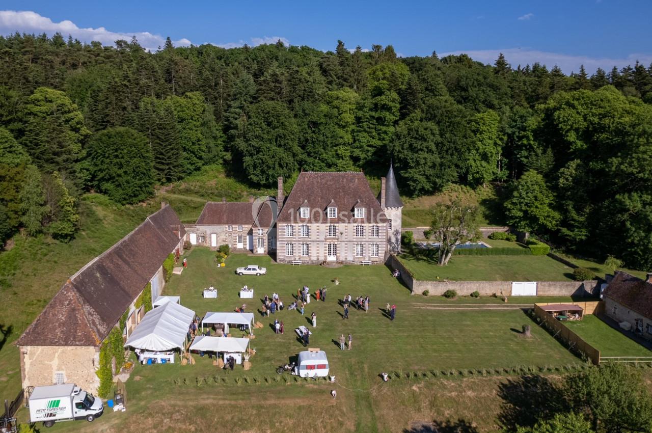 Vue aérienne d'un domaine avec un manoir, des bâtiments annexes, des tentes blanches et des personnes dans un grand jardin.