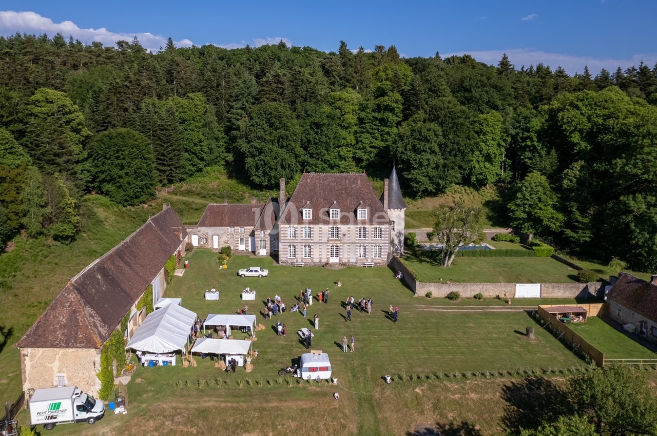 Vue aérienne d'un domaine avec un manoir, des bâtiments annexes, des tentes blanches et des personnes dans un grand jardin.