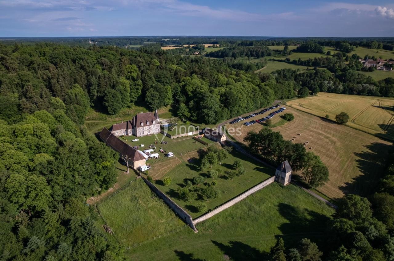 Vue aérienne d'un domaine historique entouré de verdure, avec une chapelle, des bâtiments et un parking adjacent.