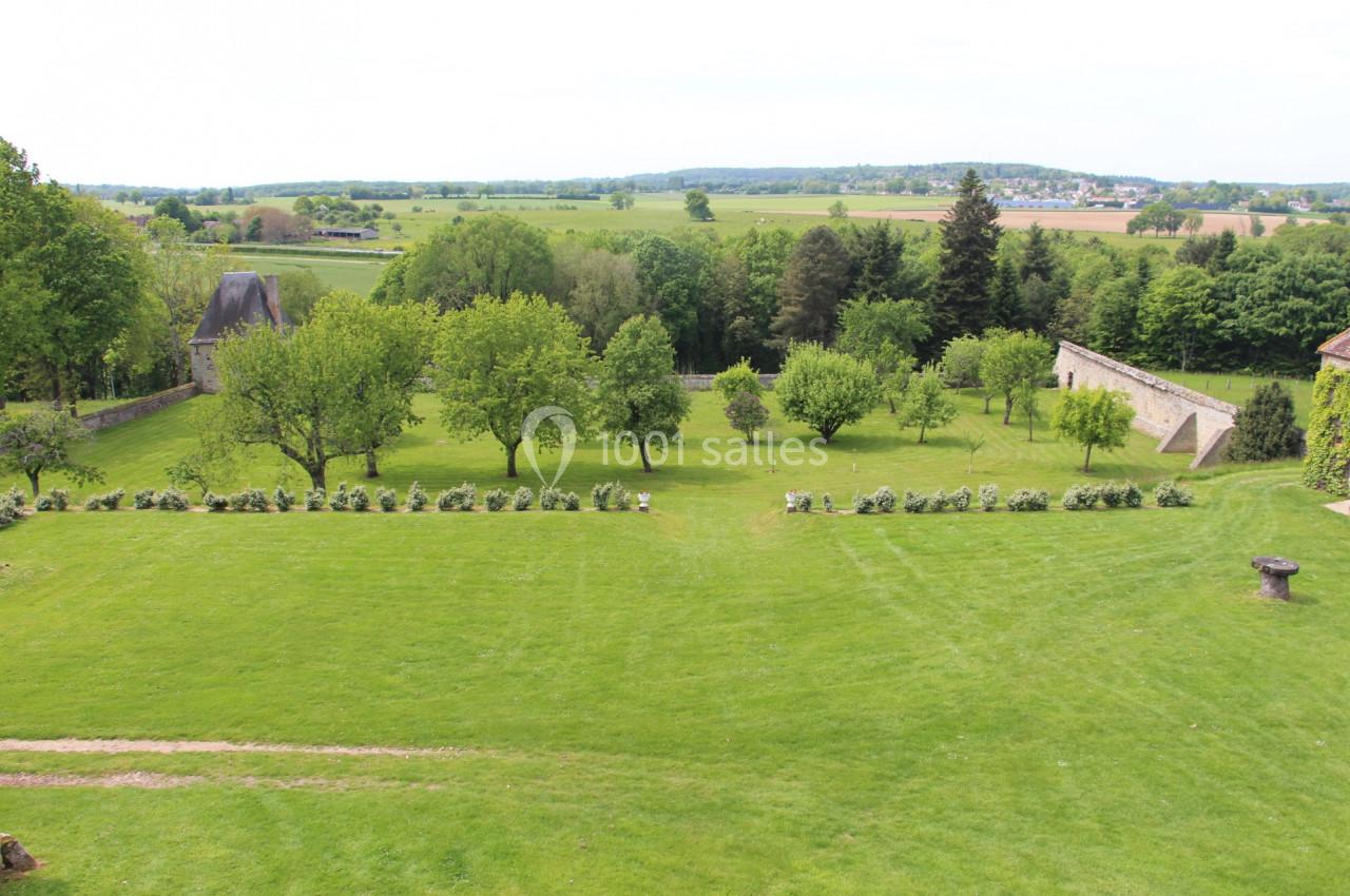 Vue d'un vaste jardin verdoyant avec des arbres, des haies et un mur de pierre en arrière-plan.