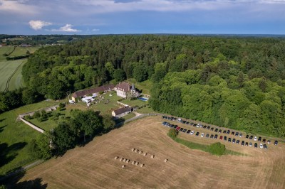 Salon rustique avec murs en pierre, canapés en cuir, table basse et porte ouverte donnant sur un jardin ensoleillé.