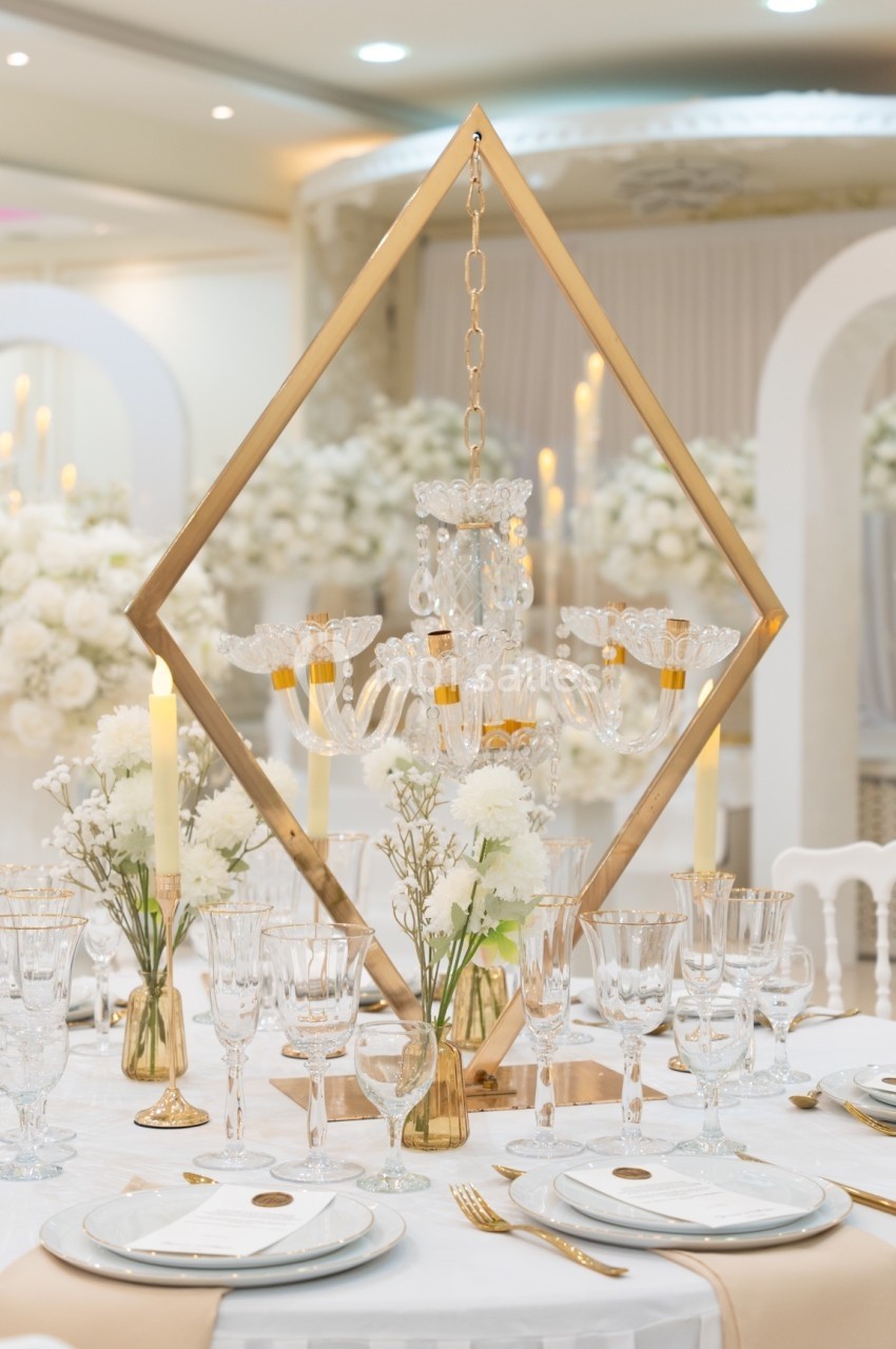 Centre de table élégant avec chandelier doré, fleurs blanches et vaisselle raffinée dans une salle de réception lumineuse.