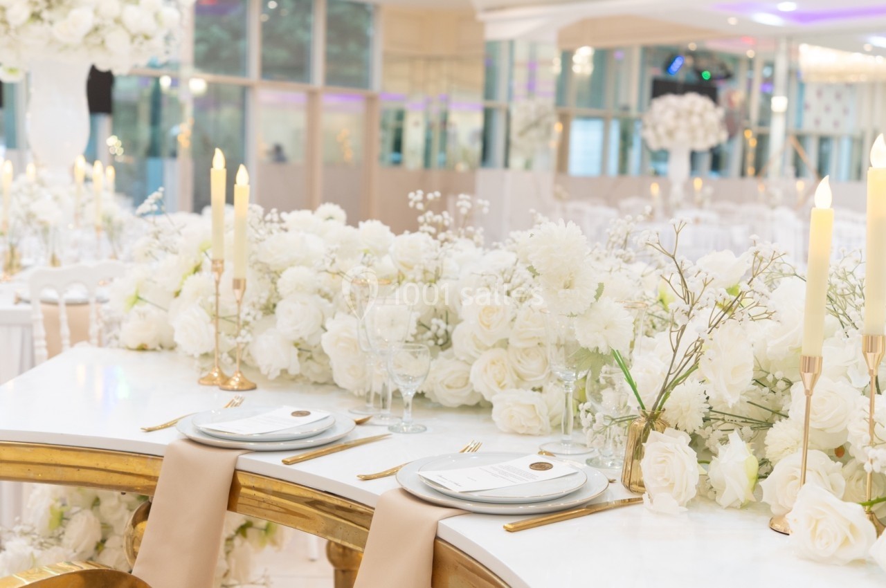 Table décorée pour un mariage avec nappes blanches, bougies, vaisselle élégante et arrangements floraux blancs.