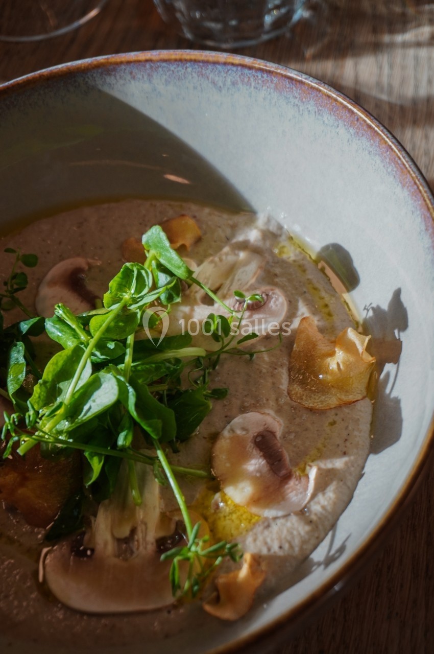 Bol de velouté garni de champignons émincés, chips croustillantes et pousses vertes, éclairé par une lumière naturelle.