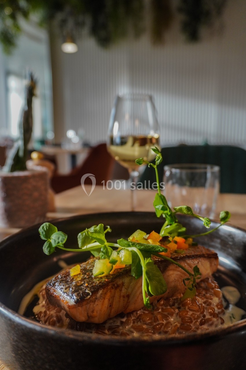 Filet de saumon grillé servi sur un lit de céréales avec des légumes colorés, dans un restaurant élégant.