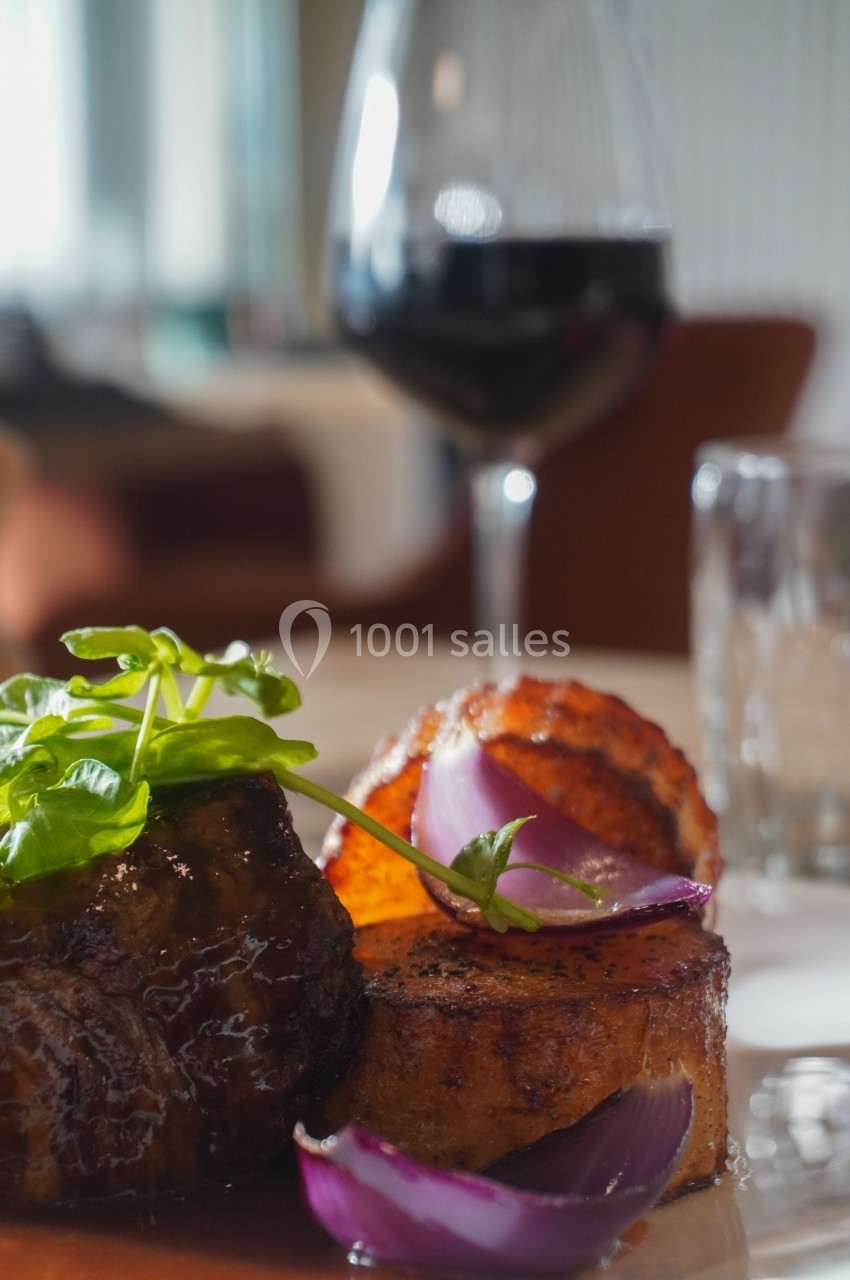 Plat de viande grillée avec des pommes de terre rôties, oignons rouges et herbes, accompagné d'un verre de vin rouge.