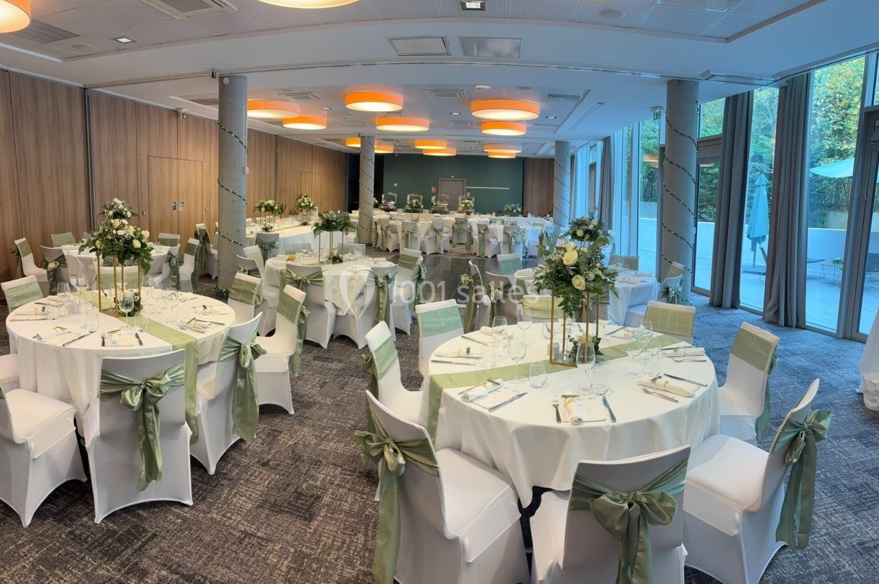 Salle de réception décorée pour un événement, avec des tables rondes ornées de nappes blanches et de rubans verts.