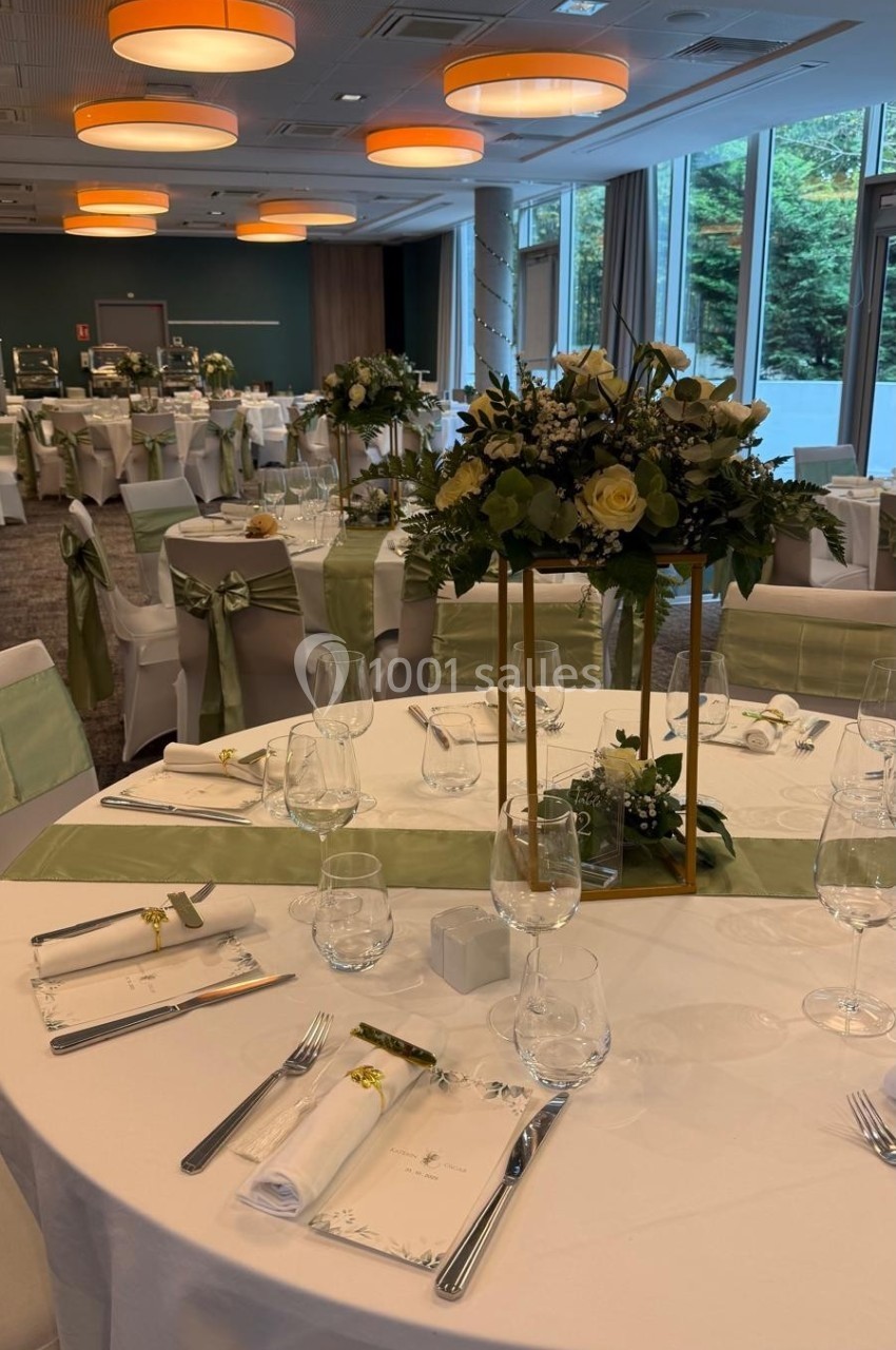 Salle de réception élégamment décorée avec des tables rondes, nappes blanches, centres de table fleuris et chaises ornées de…