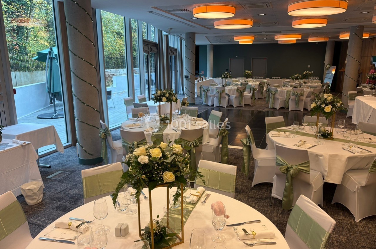 Salle de réception décorée pour un événement, avec tables rondes dressées, nappes blanches et compositions florales.