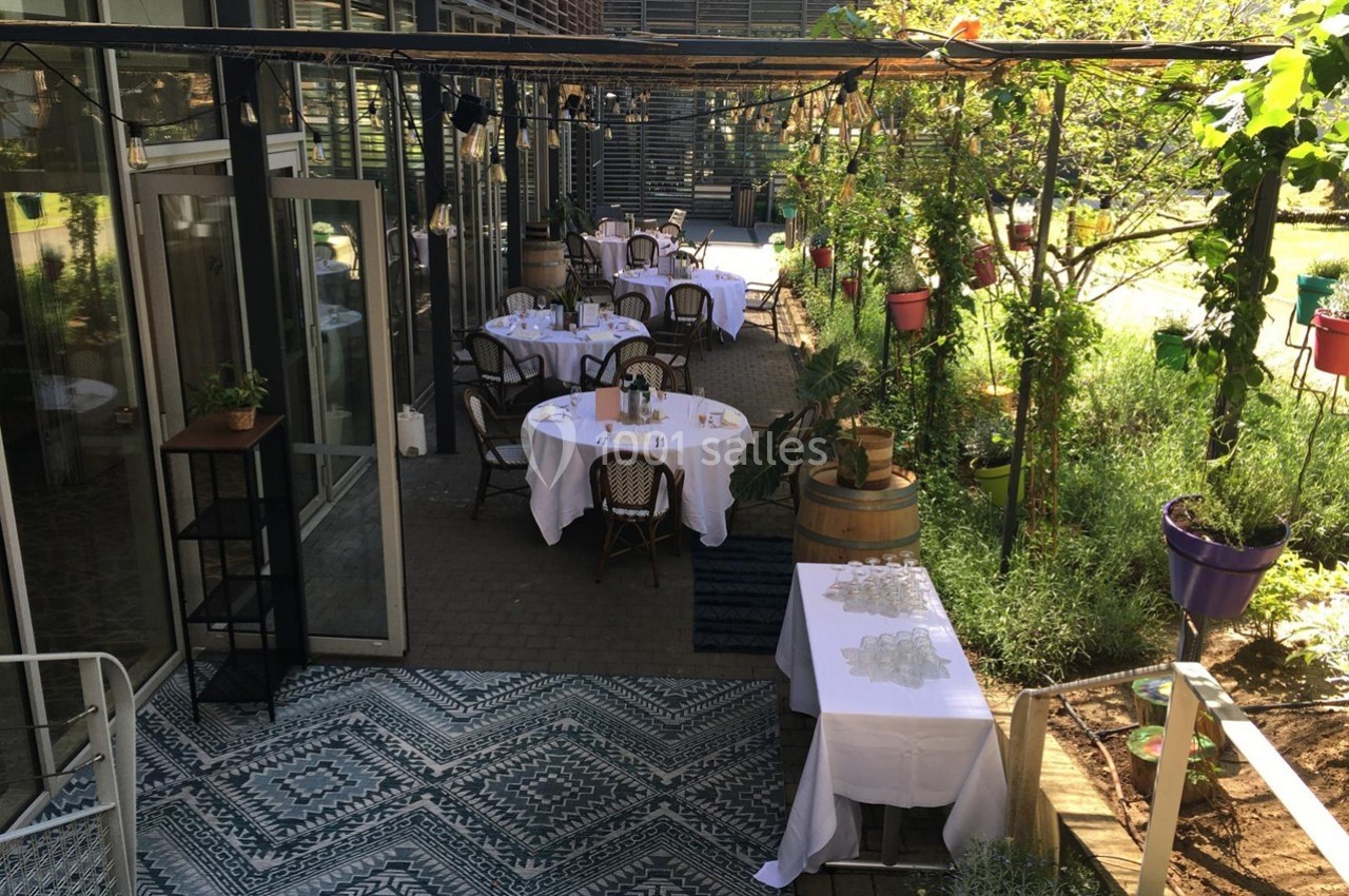 Terrasse aménagée avec des tables dressées, entourée de plantes et de verdure, sous une pergola ombragée.