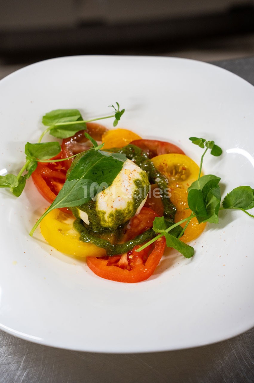 Assiette de tomates colorées avec une boule de mozzarella, sauce verte et feuilles de roquette.
