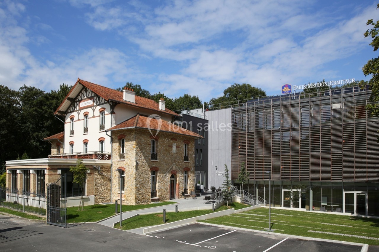 Bâtiment ancien en pierre rénové à côté d'une structure moderne avec façade en bois, entourés de verdure.