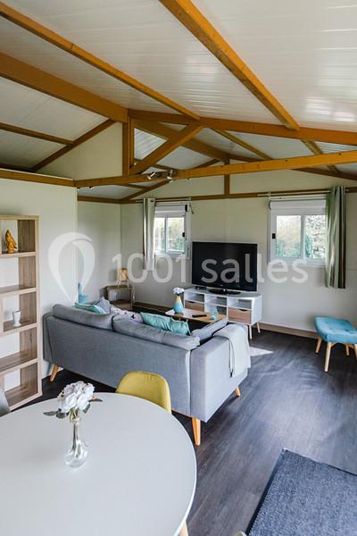 Intérieur lumineux d'un salon avec canapé, télévision, table ronde et étagères, dans un espace au plafond en bois.