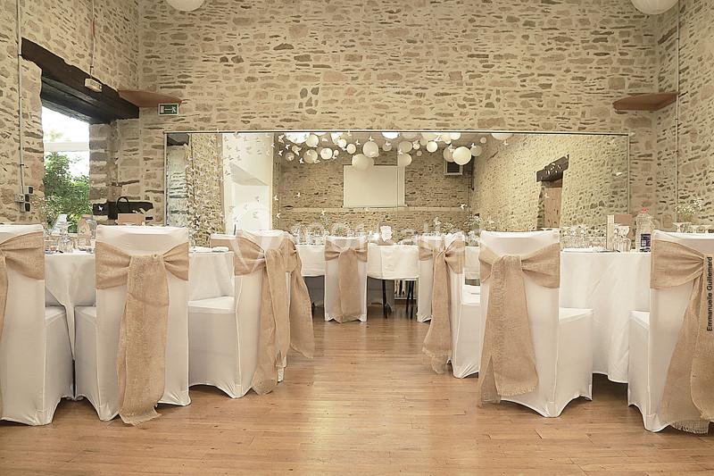 Salle de réception décorée avec des chaises blanches ornées de nœuds en toile de jute et des guirlandes lumineuses…