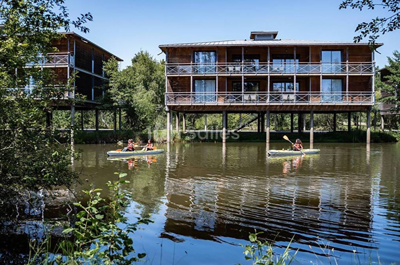 Des cabanes en bois sur pilotis au bord d'un étang, avec des personnes en canoë sur l'eau.