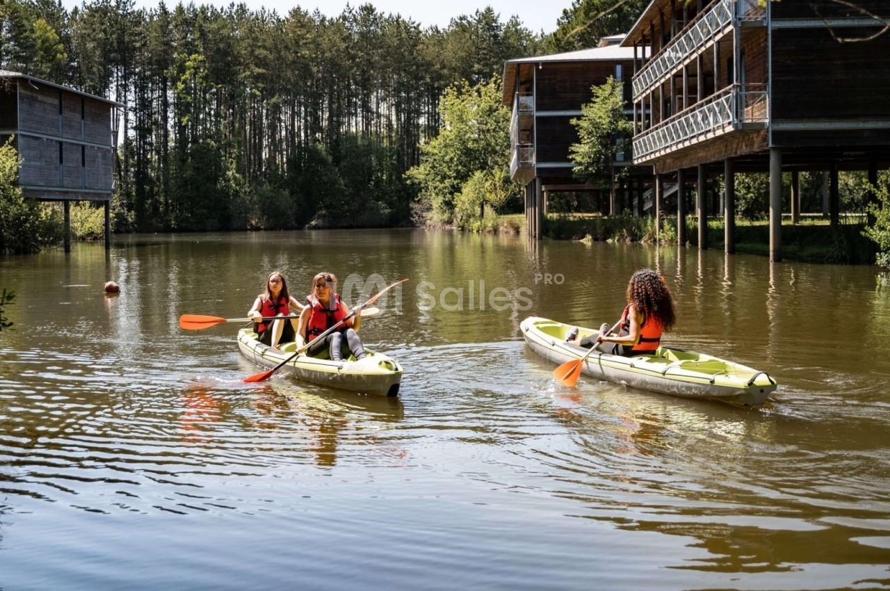 Trois personnes pagayant en kayak sur un lac entouré de cabanes en bois et d'arbres.