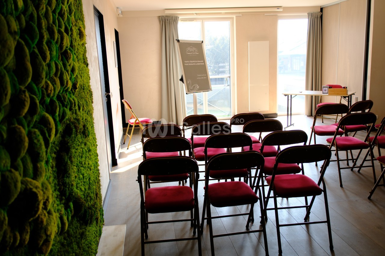 Salle de réunion lumineuse avec des chaises pliantes alignées, un tableau de présentation et un mur végétal.