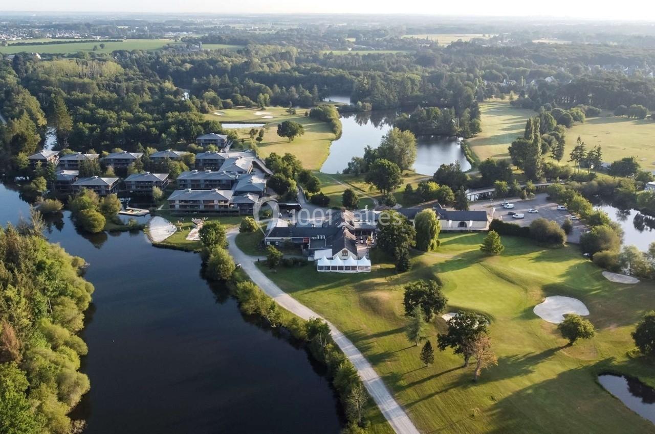 Vue aérienne d'un complexe avec bâtiments, lacs, terrains de golf et espaces verts entourés de forêts.