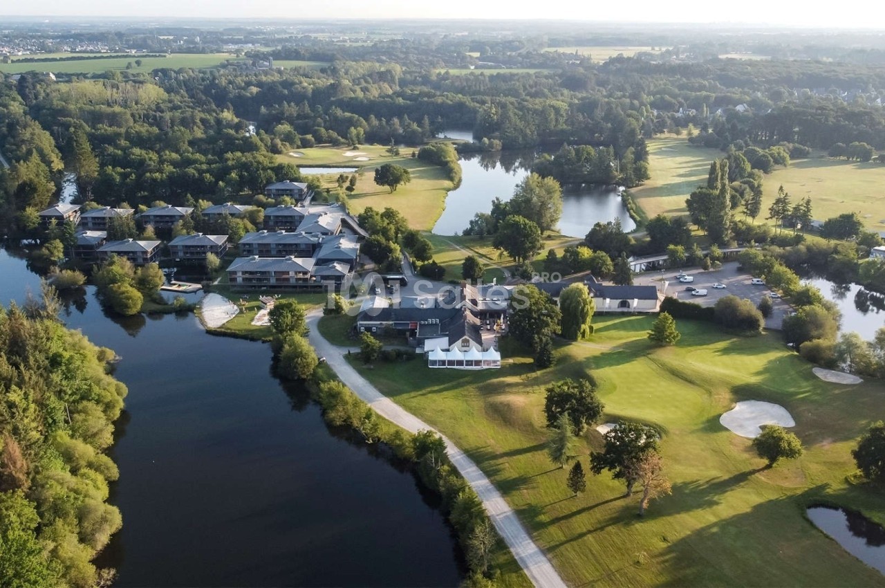 Vue aérienne d'un complexe avec bâtiments, lacs, terrains de golf et espaces verts entourés de forêts.