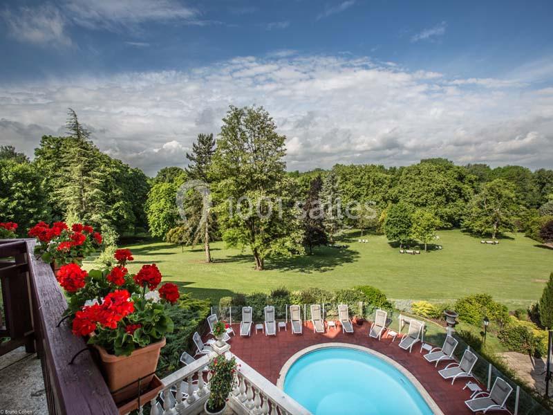 Vue d'une piscine entourée de chaises longues, avec un grand jardin verdoyant et des arbres en arrière-plan.