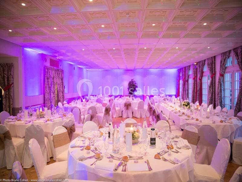 Salle de réception décorée avec des tables rondes dressées, nappes blanches et éclairage d'ambiance violet.