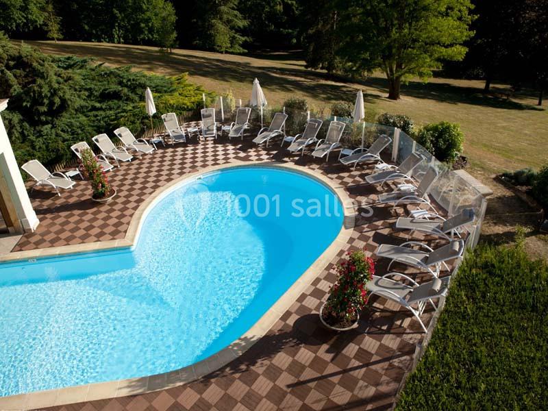 Piscine extérieure en forme de cœur entourée de transats, parasols et végétation dans un jardin arboré.