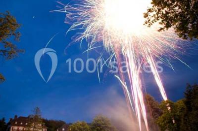 Chambre lumineuse avec parquet en bois, lit double, canapé rouge, table basse et grandes fenêtres avec rideaux fleuris.