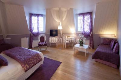 Chambre lumineuse avec parquet en bois, lit double, canapé rouge, table basse et grandes fenêtres avec rideaux fleuris.