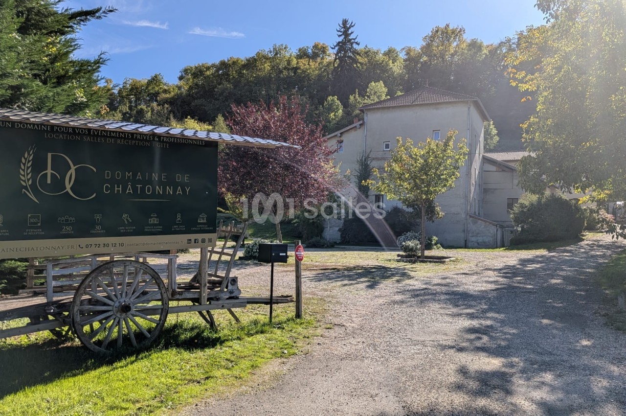 Panneau du Domaine de Châtonnay sur une charrette en bois, devant un chemin menant à des bâtiments entourés de verdure.