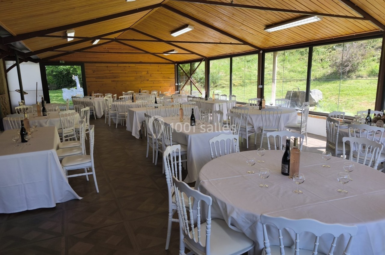 Salle de réception lumineuse avec tables rondes et rectangulaires dressées, chaises blanches et vue sur l'extérieur…