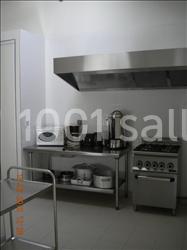 Cuisine équipée avec un four, une plaque de cuisson, un micro-ondes, une cafetière et des ustensiles sur un plan de travail.