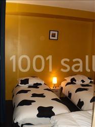 Deux lits simples avec des housses de couette à motif noir et blanc, éclairés par une lampe de chevet dans une chambre jaune.