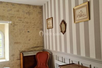 Pressoir ancien en bois dans une pièce avec murs en pierre, plafond à poutres apparentes et sol en parquet.