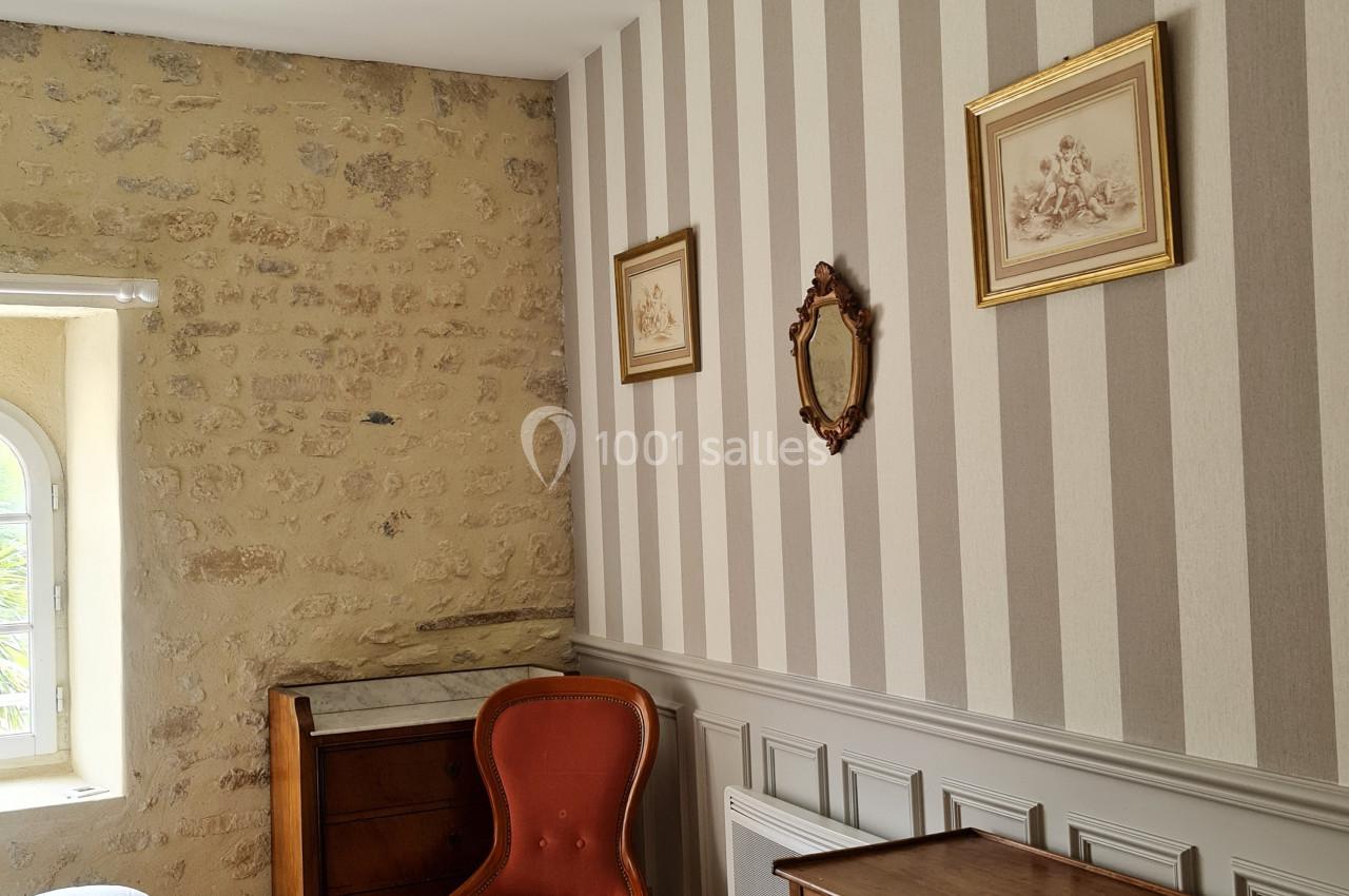Chambre avec mur en pierre et papier peint rayé, mobilier ancien comprenant une chaise, une table et un petit meuble.