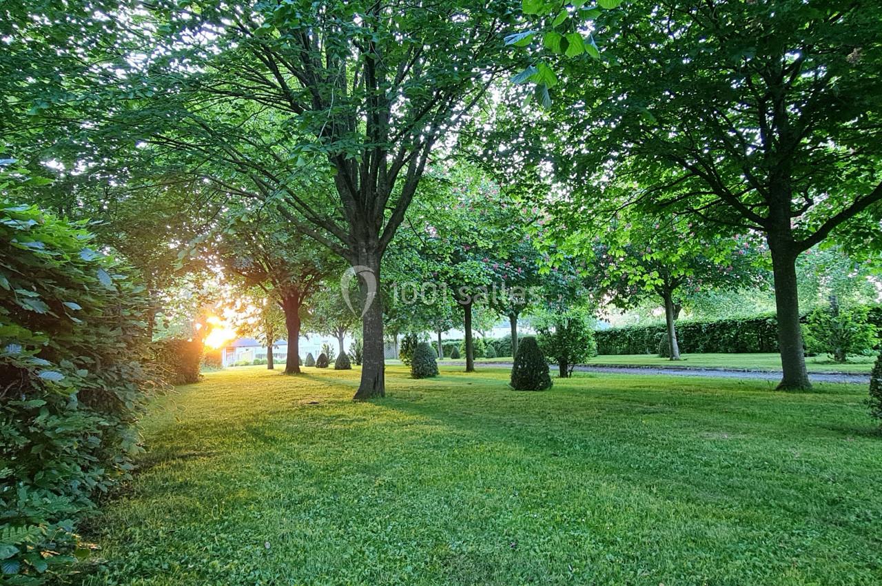 Pelouse verdoyante bordée d'arbres et de haies, éclairée par une lumière de coucher de soleil.