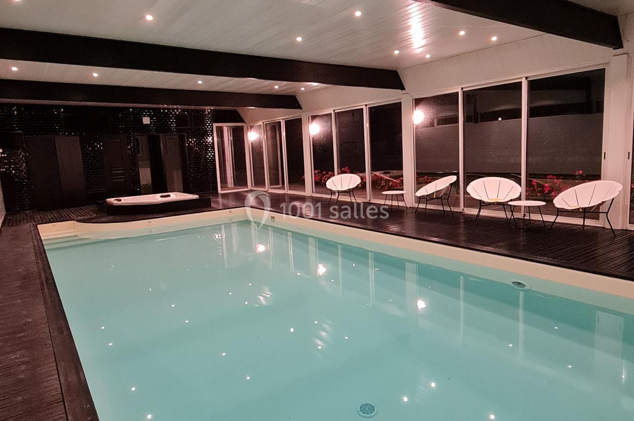 Piscine intérieure éclairée entourée de chaises modernes et de baies vitrées donnant sur un espace extérieur.